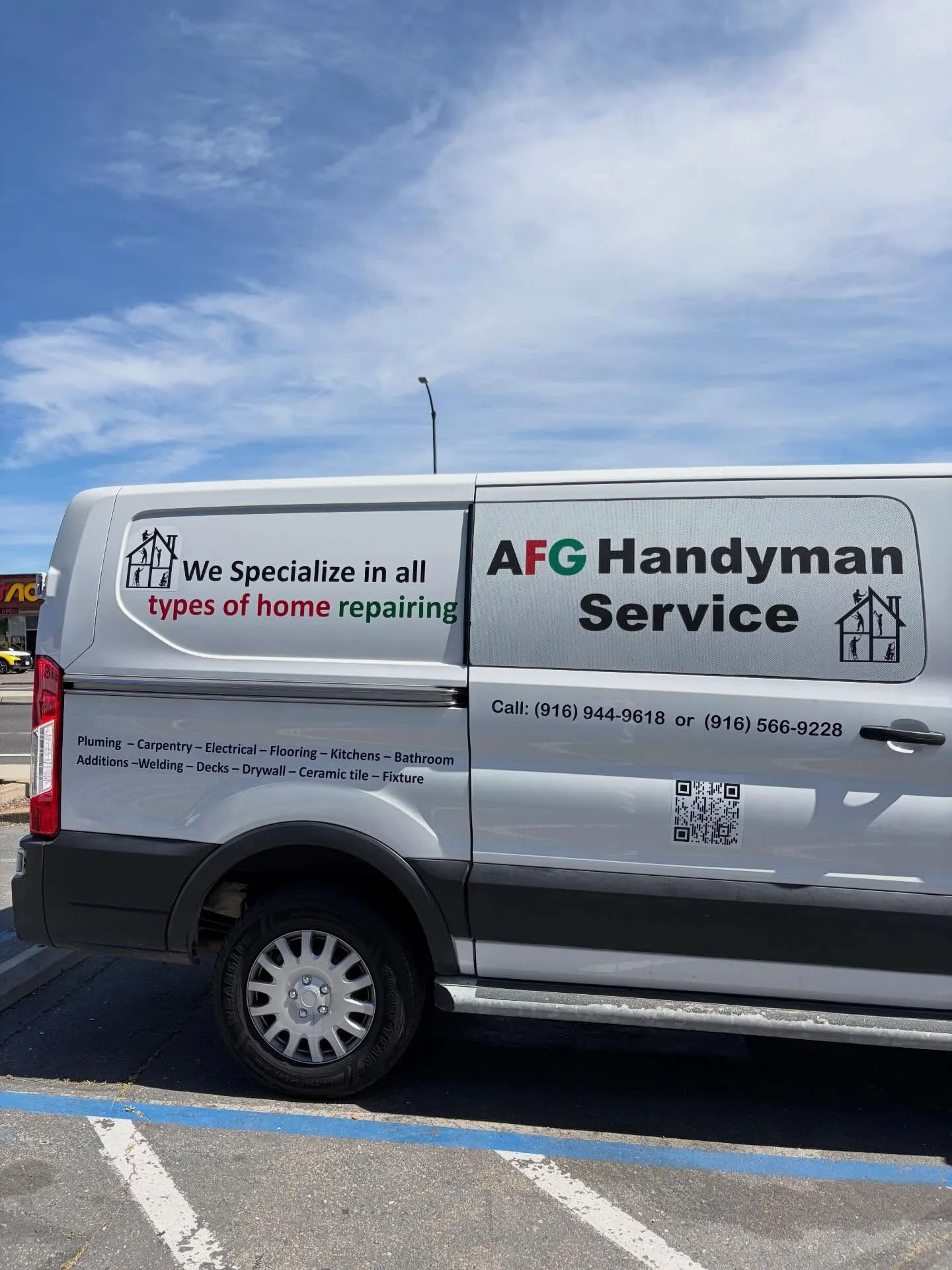 Rear-quarter side view of the white AFG Handyman Service van showing full vinyl graphics with service list, phone numbers, and QR code