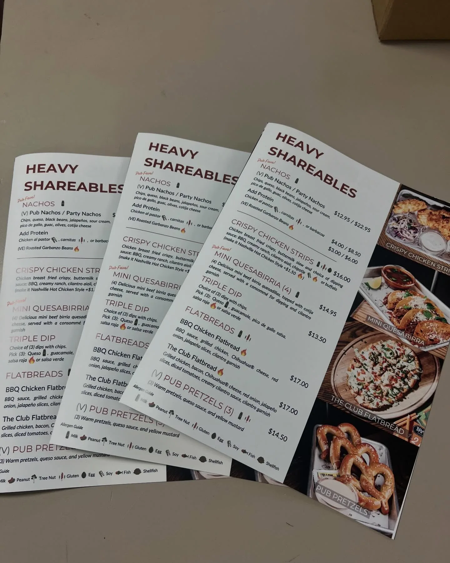 Three overlapping printed restaurant menu panels titled Heavy Shareables with food photos of chicken strips, quesabirria, flatbread, and