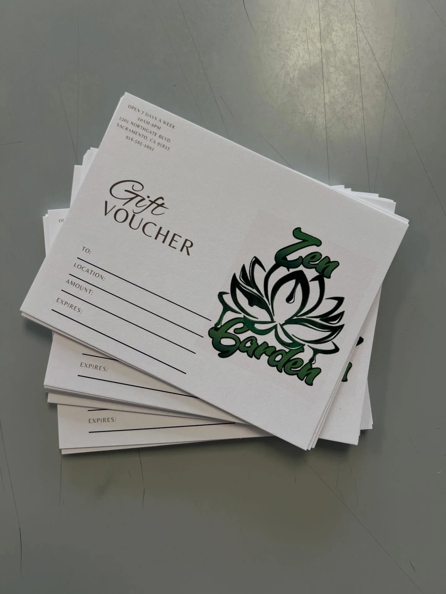 A stack of printed gift voucher cards for Zen Garden (2201 Northgate Blvd, Sacramento) with a green lotus logo, fanned out on a gray work