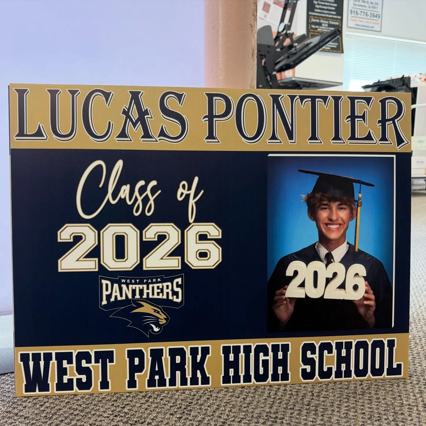 A navy-and-gold personalized graduation yard sign for 'Lucas Pontier, Class of 2026, West Park High School' with the student's cap-and-gown