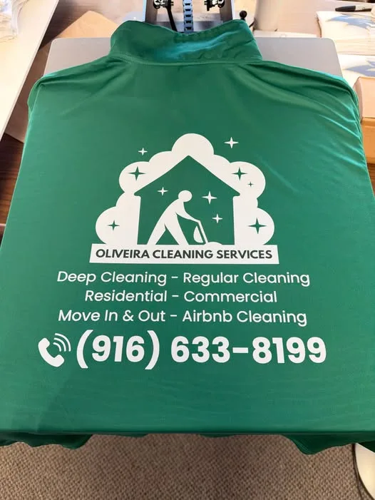 A green quarter-zip shirt laid on a heat press with a freshly applied white back print for Oliveira Cleaning Services, including a
