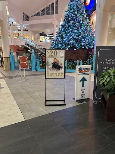 Freestanding poster sign stand and a printed directional floor sign installed inside a shopping mall near a Christmas tree, advertising the