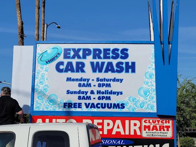 Large outdoor pole sign for Harv's Express Car Wash with bubble graphics and hours, mounted above red Auto Repair and Clutch Mart signage.